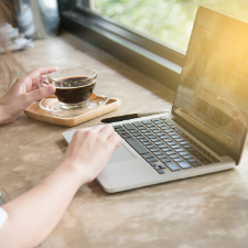 woman's hands reaching for laptop and clear mug of coffee on a table