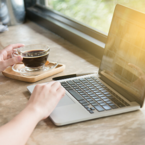 woman's hands reaching for laptop and clear mug of coffee on a table