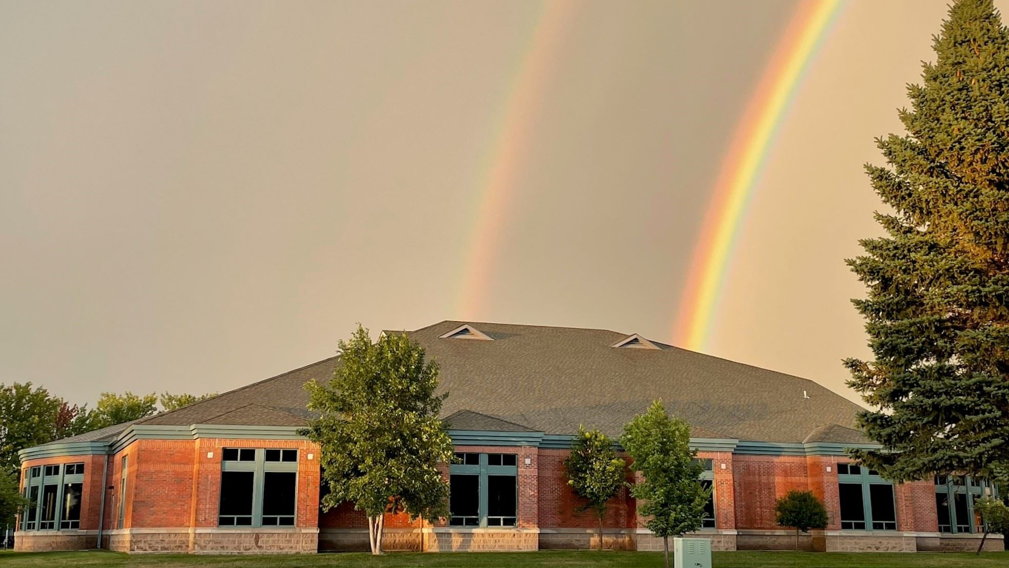 A wide exterior photo of the library building haloed by a beautiful double rainbow
